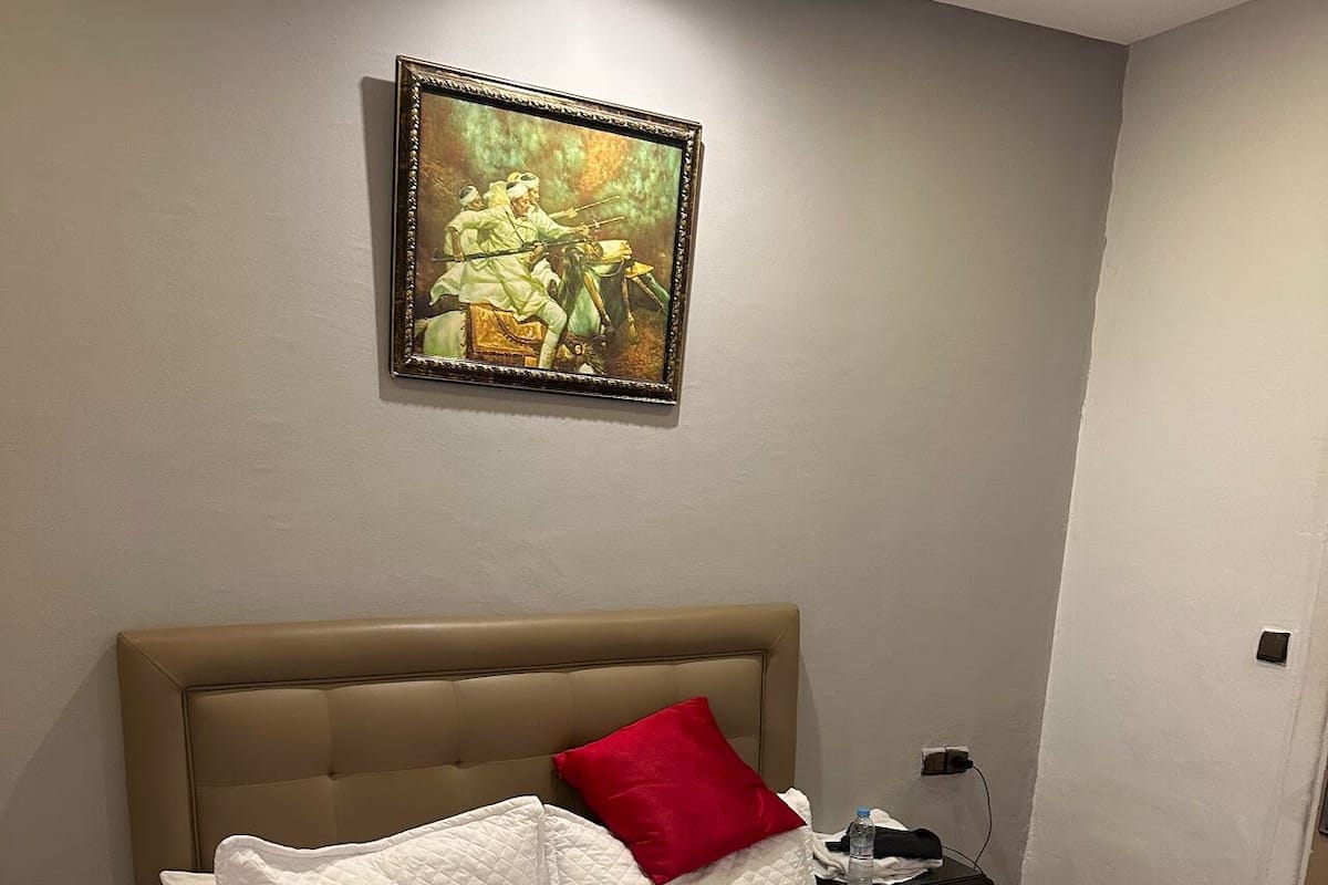 Un dormitorio con una cama, una mesita de noche, una lámpara y un cuadro en la pared.