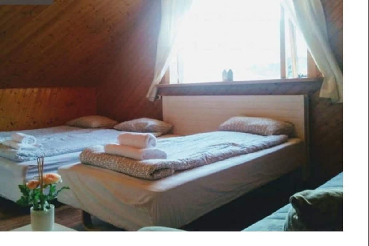 A cozy room with two beds, a window with curtains, and a vase with flowers.