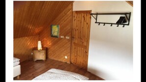 A cozy attic bedroom with wooden walls, a bed, a nightstand, and a wall-mounted shelf. - Gabriel Guesthouse (Vestmannaeyjar)