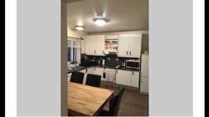 A compact kitchen with white cabinets, a microwave, and a dining table with chairs. - Gabriel Guesthouse (Vestmannaeyjar)