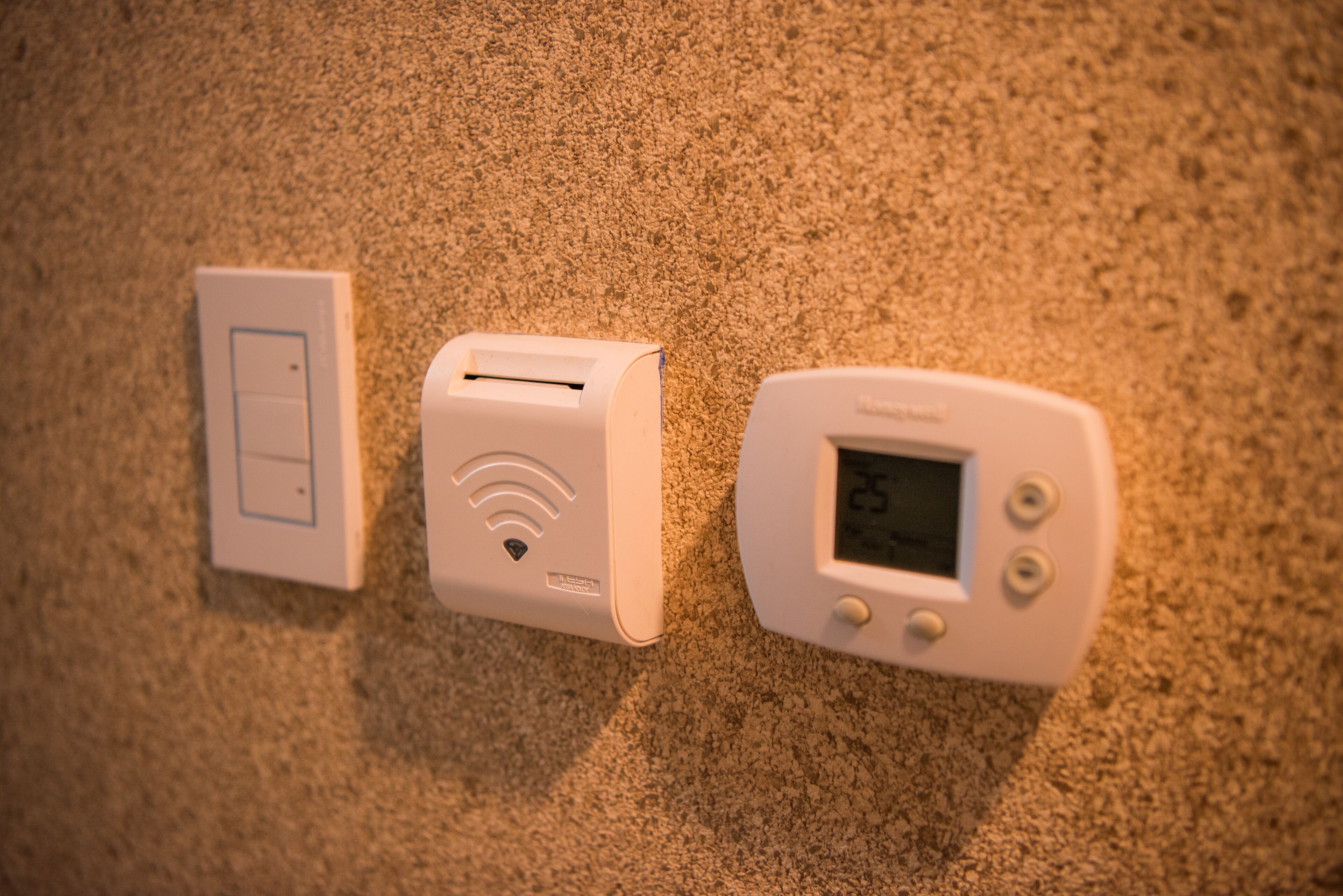 Tres dispositivos montados en la pared: un interruptor de luz, un router Wi-Fi y un termostato.