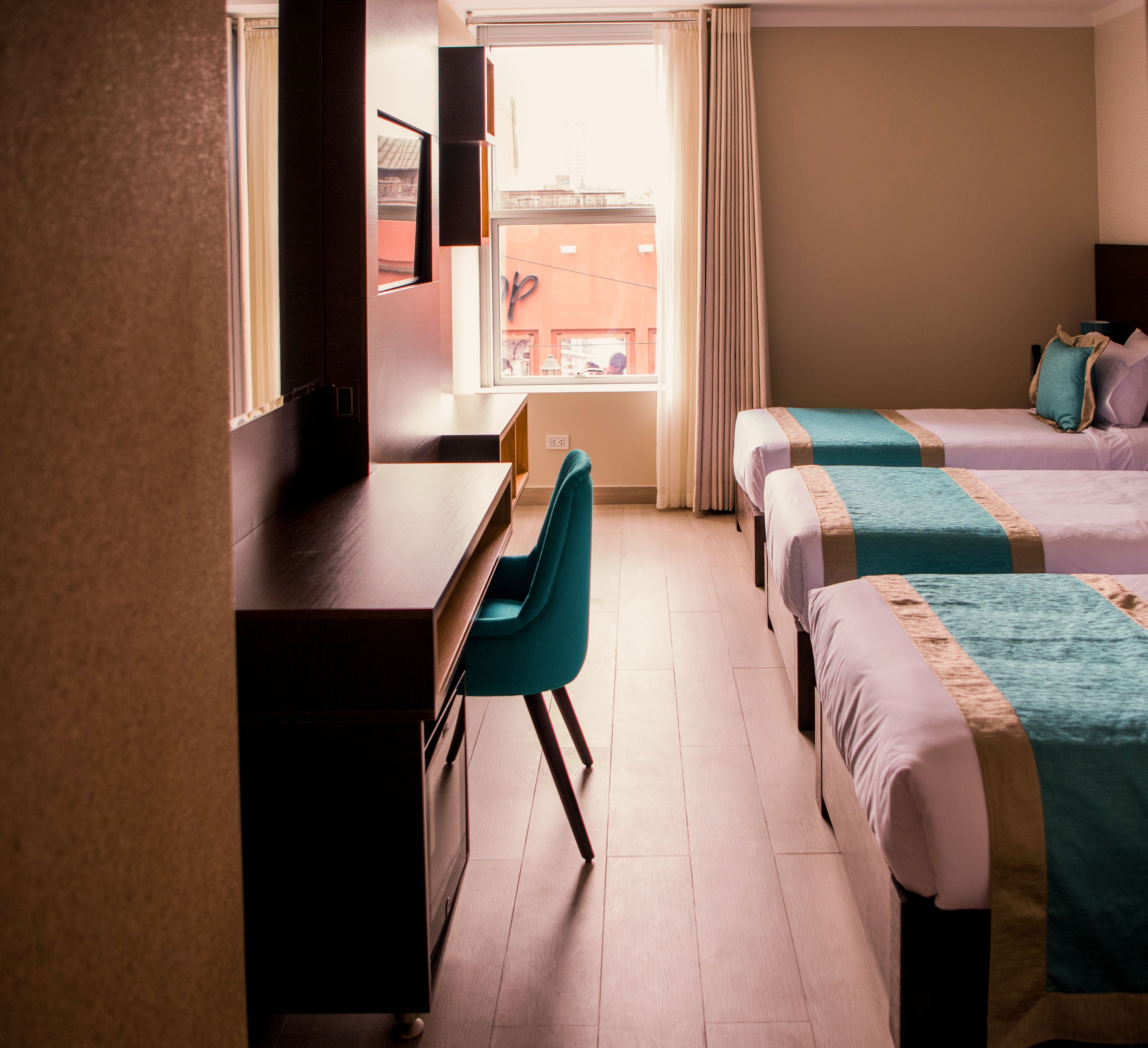 Une chambre d’hôtel équipée d’un bureau, de deux lits, d’une chaise et d’une fenêtre avec des rideaux.