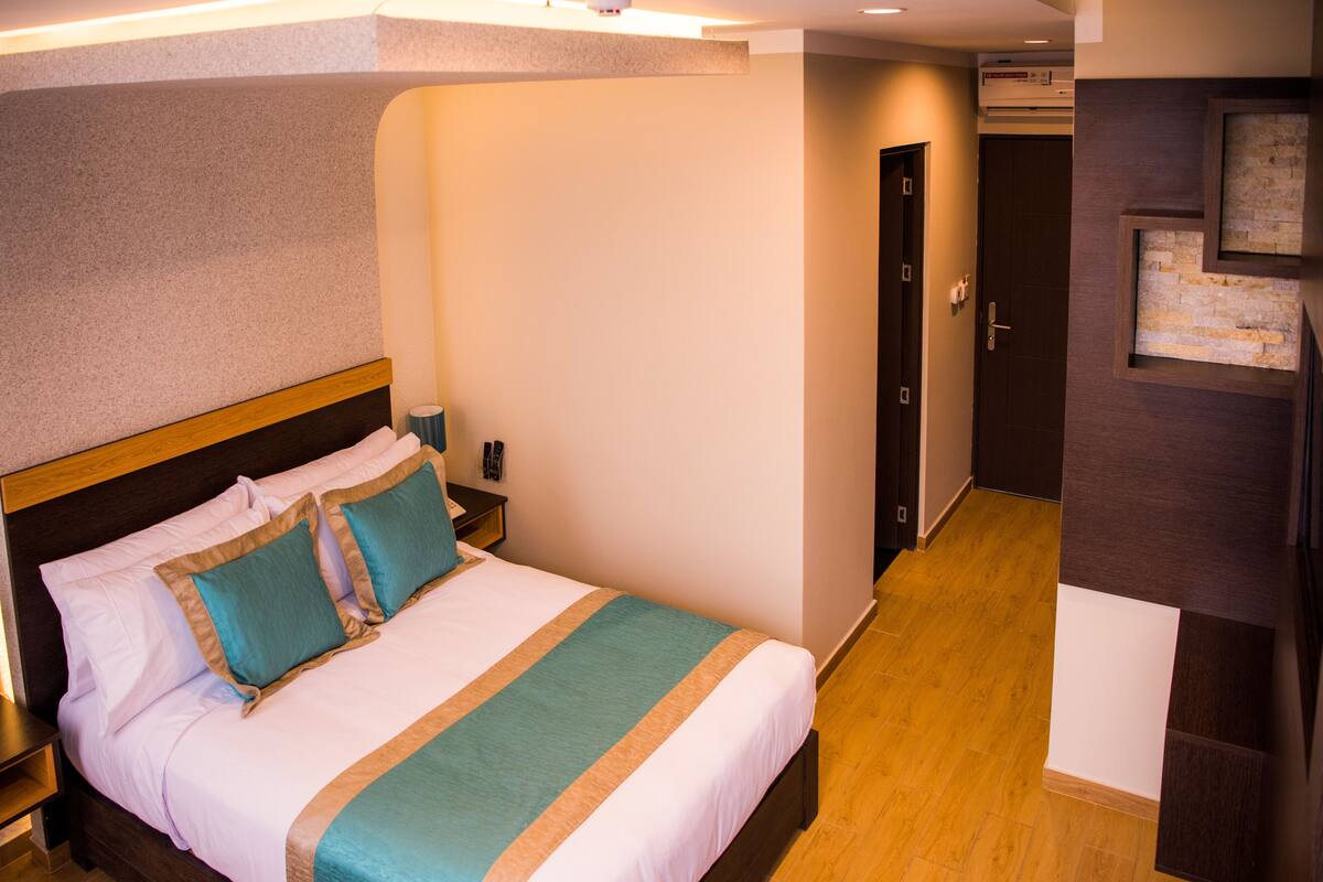 Quarto de hotel com uma cama grande, cabeceira de madeira e uma mesa de cabeceira.