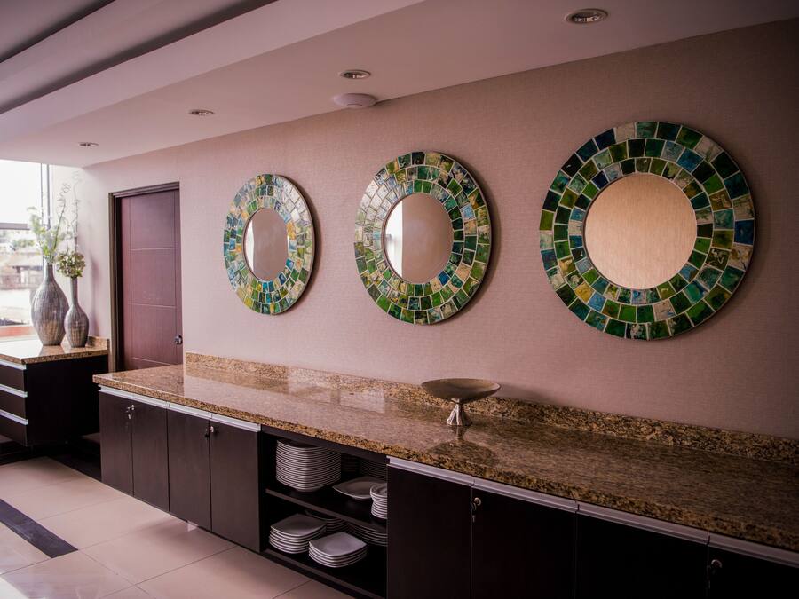 A modern kitchen with a granite countertop, dark cabinets, and three mosaic mirrors on the wall.