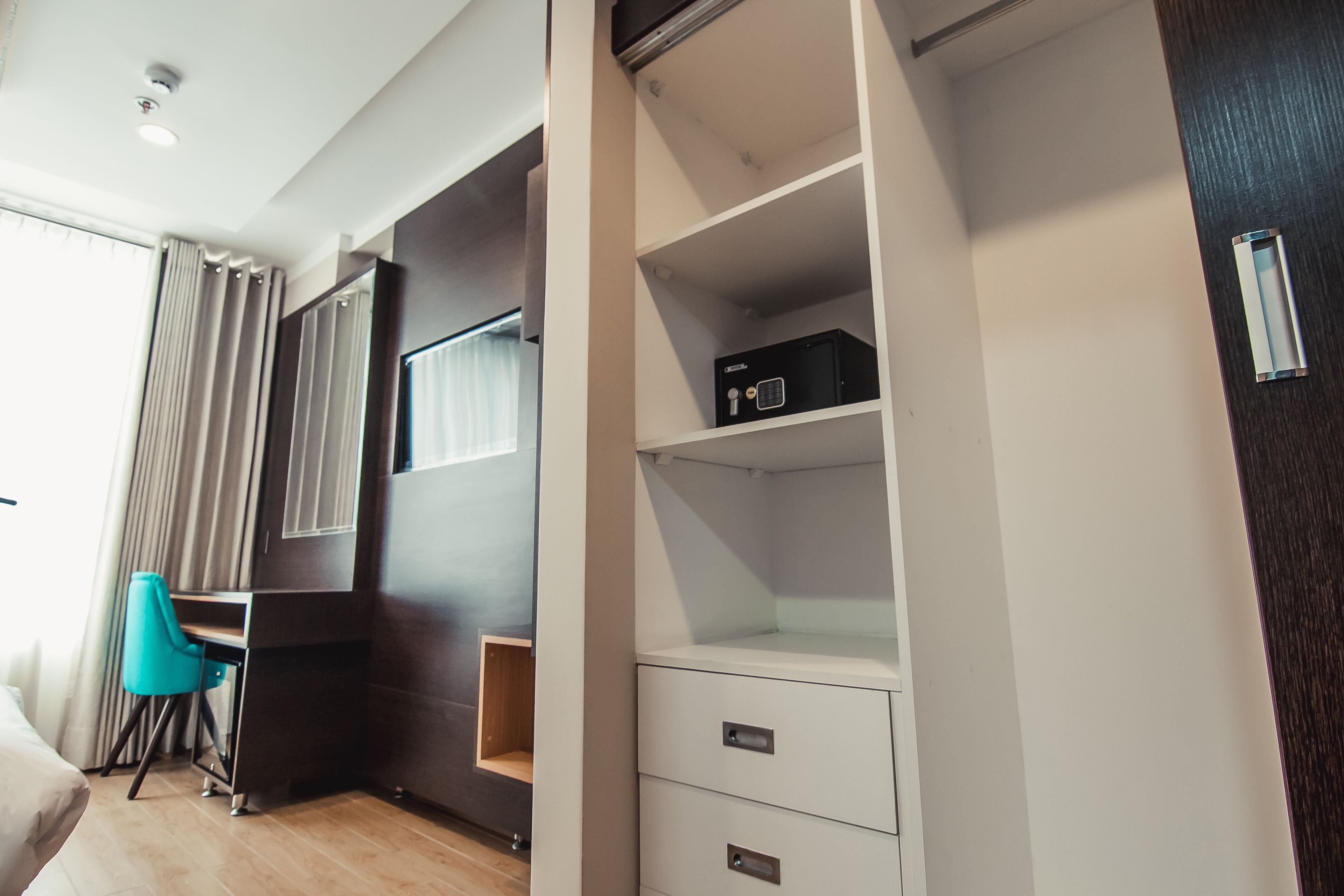 A hotel room with a bed, a desk, a chair, a wardrobe, and a window with curtains.