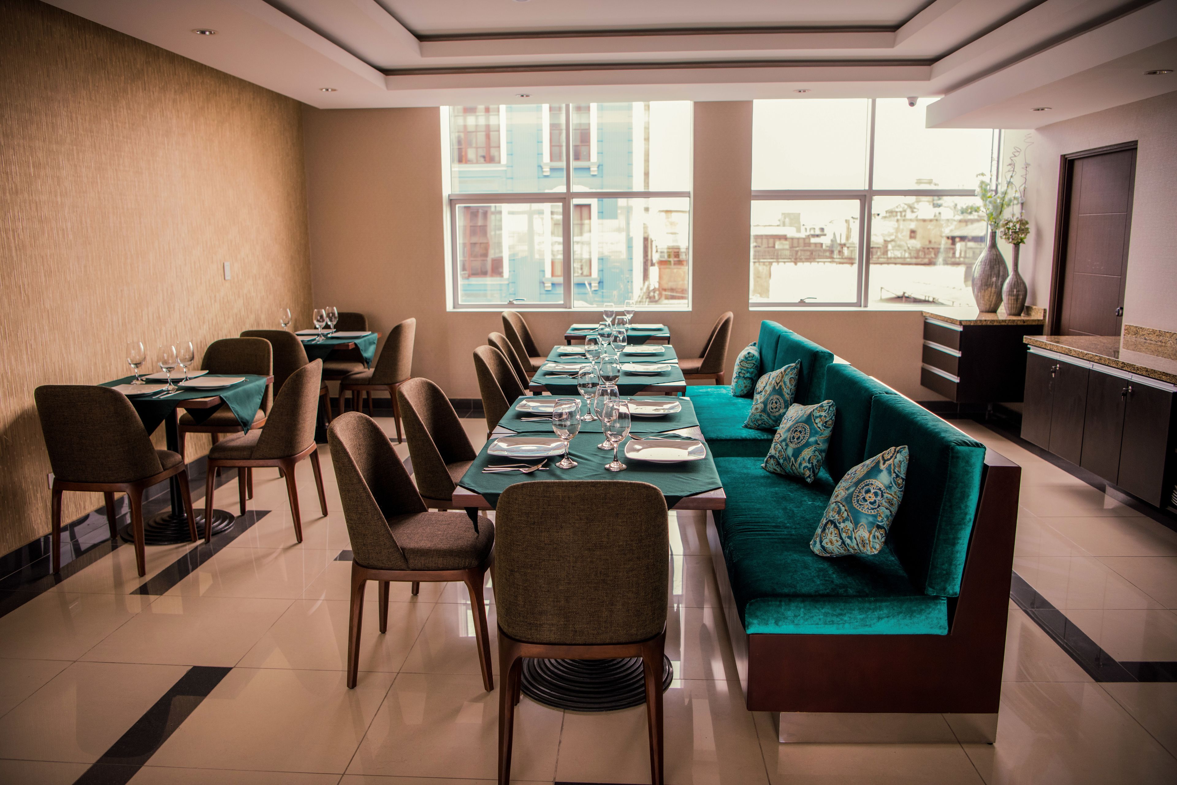 A dining area with a long table set for six, surrounded by chairs and a sofa with patterned cushions.