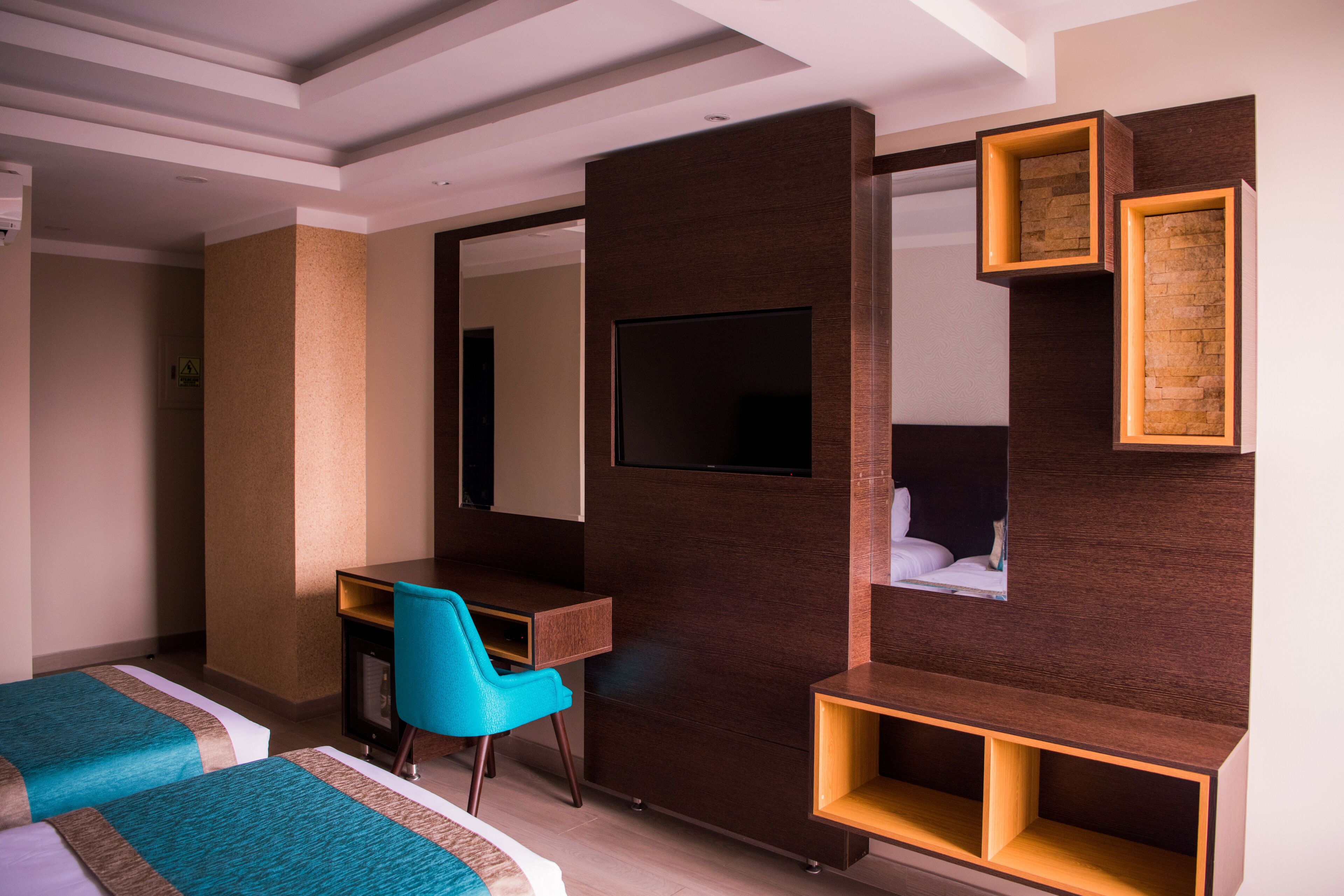 Habitación de hotel con dos camas, un escritorio, una silla, televisor y estanterías empotradas.