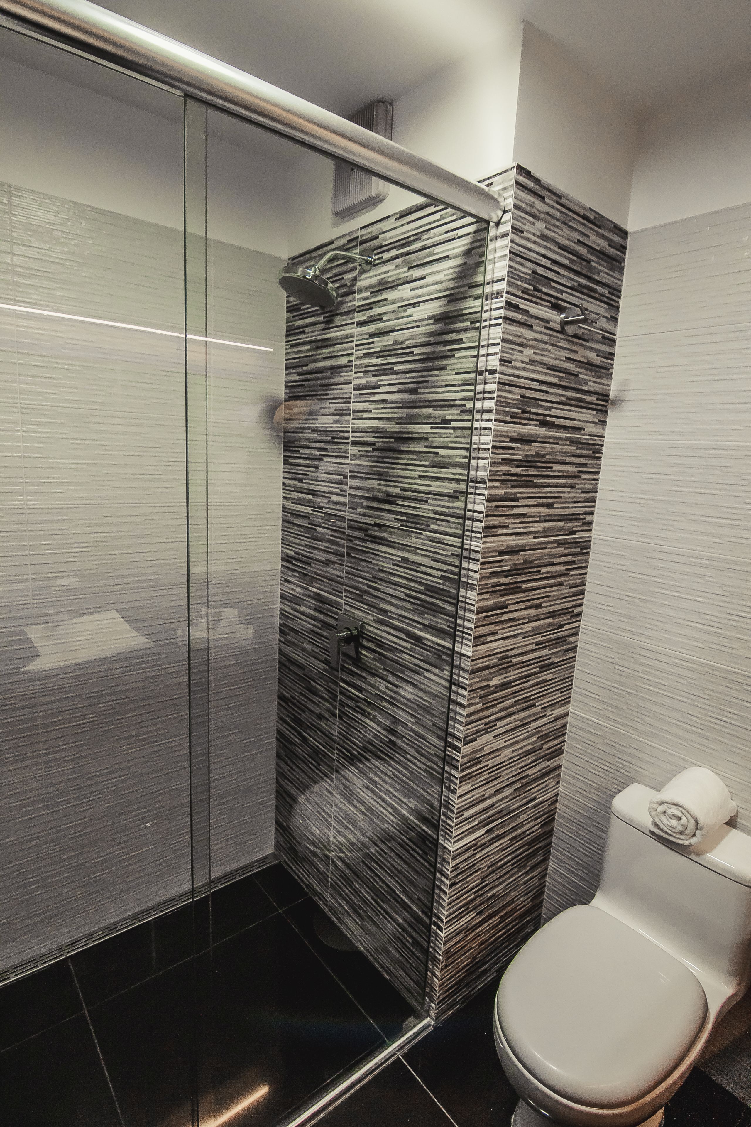 A modern bathroom with a glass shower enclosure, a toilet, and a wall with a textured pattern.