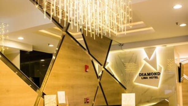 Een modern receptiebalie met een geometrisch ontwerp en een kroonluchter erboven. Op de muur staat de naam 'DIAMOND LIMA HOTEL'.