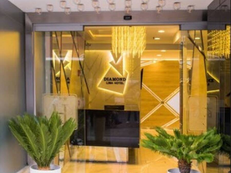 Exterior do Hotel Diamond Lima, com fachada moderna, grande entrada de vidro e duas plantas em vasos na entrada.