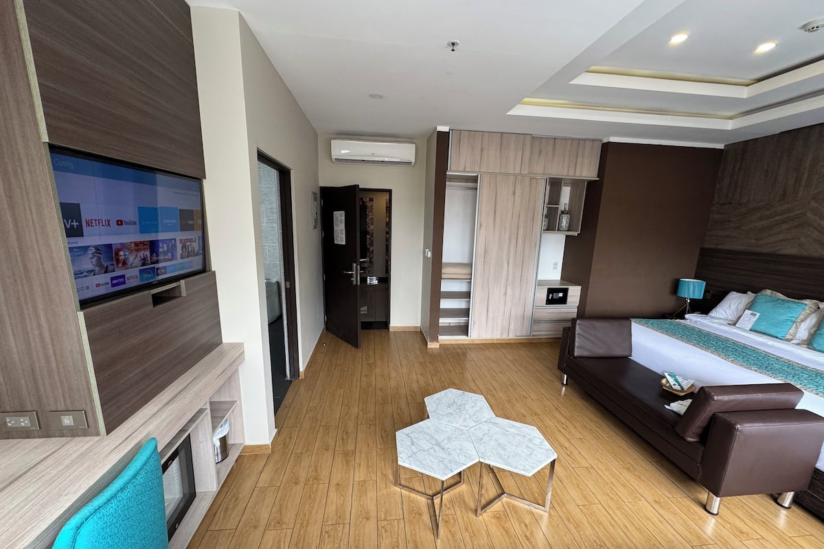 Quarto de hotel moderno com televisão de tela plana, sofá-cama, mesa de centro pequena e escada para uma varanda.