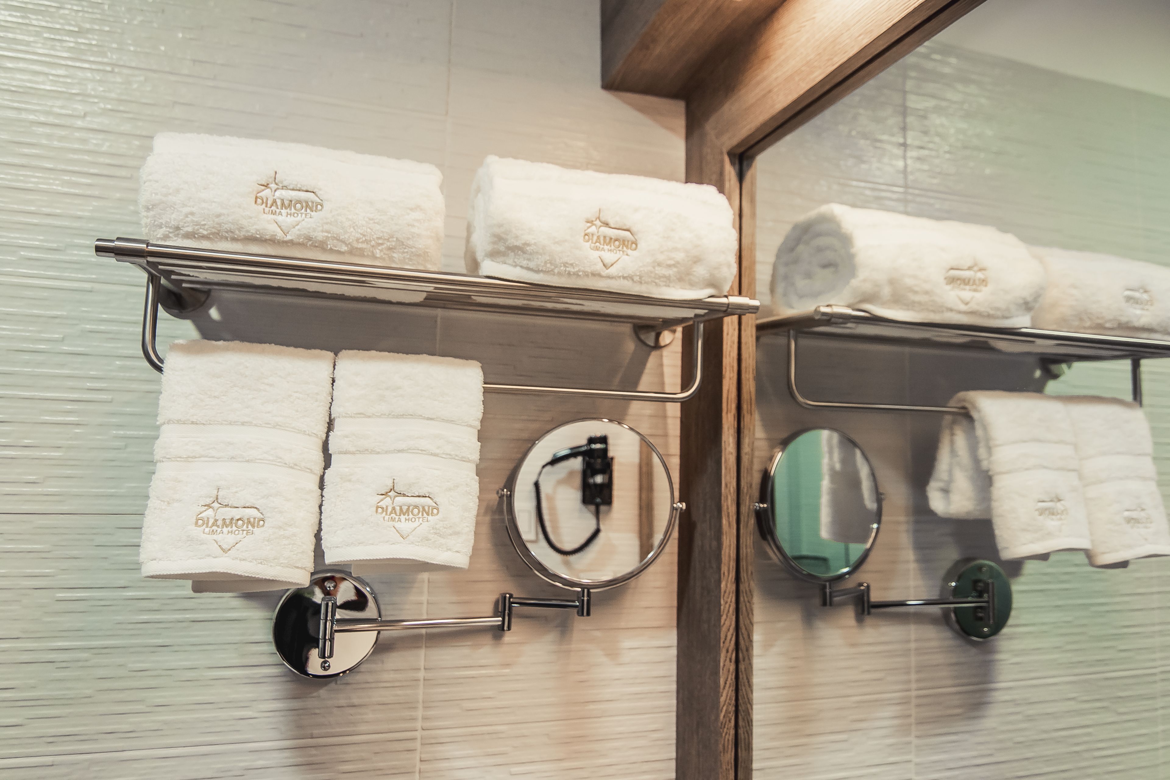 A bathroom with a towel rack holding several white towels with "Diamond Luma Hotel" branding.