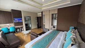 Een moderne hotelkamer met een groot bed, een bank, een televisie, een bureau en een badkamer die door een geopende deur zichtbaar is.
