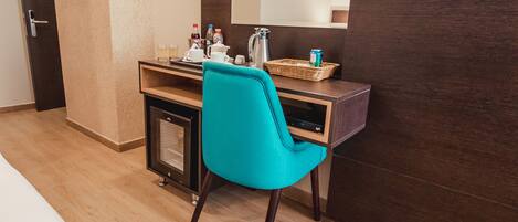 Habitación de hotel con un escritorio de madera, una silla color turquesa, un mueble pequeño, un televisor y un espejo.