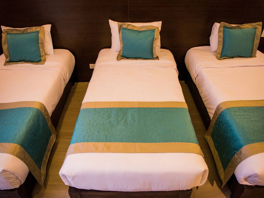Tres camas individuales con cubrecamas verde azulado y color beige, un cabecero de madera y una mesita de noche con un teléfono.