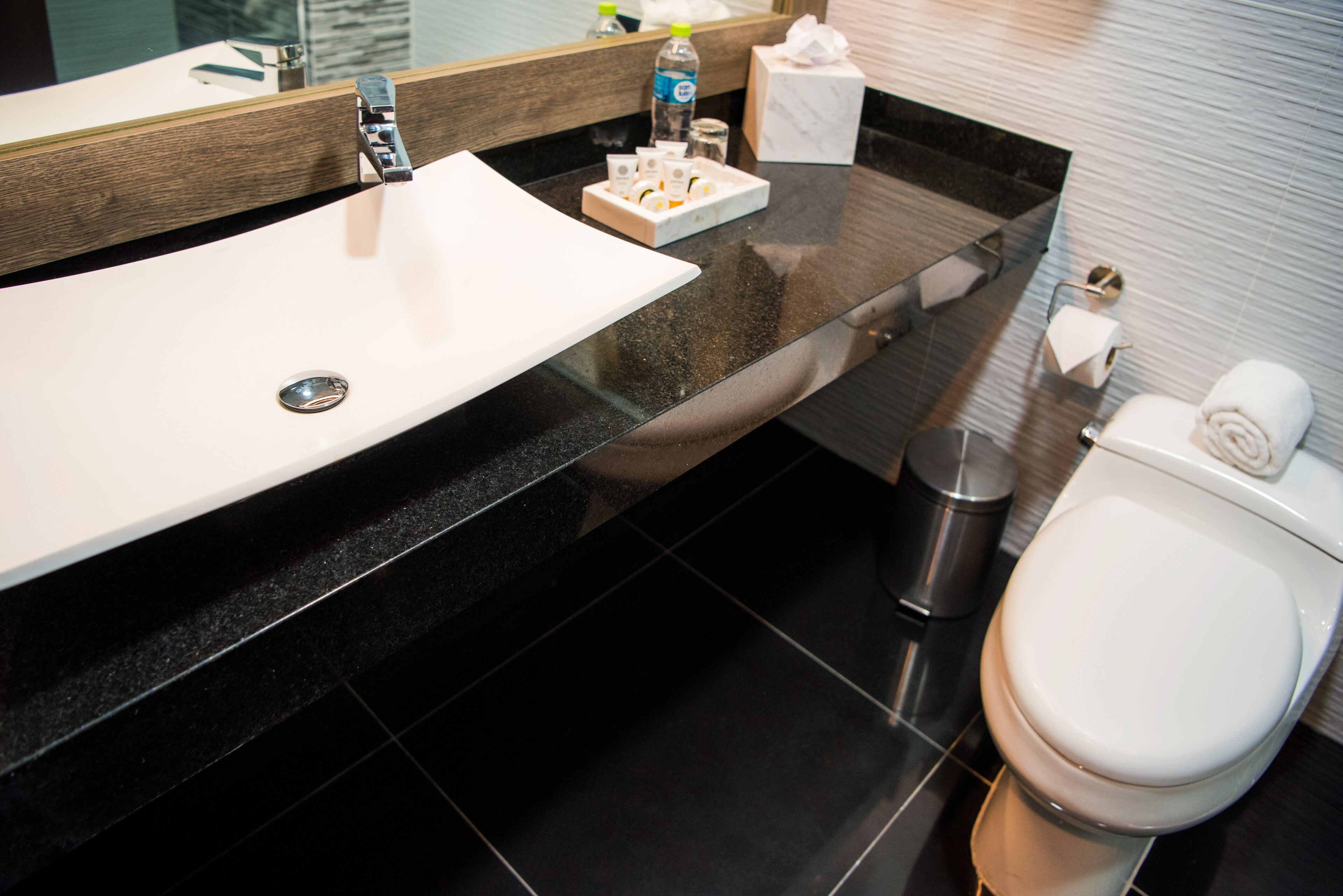 A modern bathroom with a white sink, black countertop, and a white toilet.