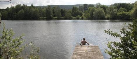 Une jetée en bois s’étendant sur un lac paisible, entouré d’une végétation luxuriante et avec des collines en arrière-plan.