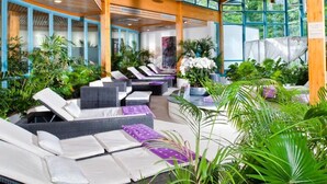 A sun lounge area with multiple seating options, surrounded by lush greenery and large windows.