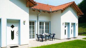 A white building with a red-tiled roof, a covered patio with a table and chairs, and a number '6' on the door.
