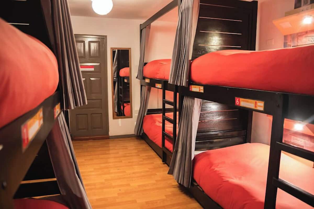 Una habitación con literas, suelo de madera, una puerta y un espejo.