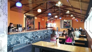A restaurant interior with wooden tables and benches, a counter with a coffee machine, and hanging pendant lights. - Pariwana Hostel Cusco - Adults only (Cusco)
