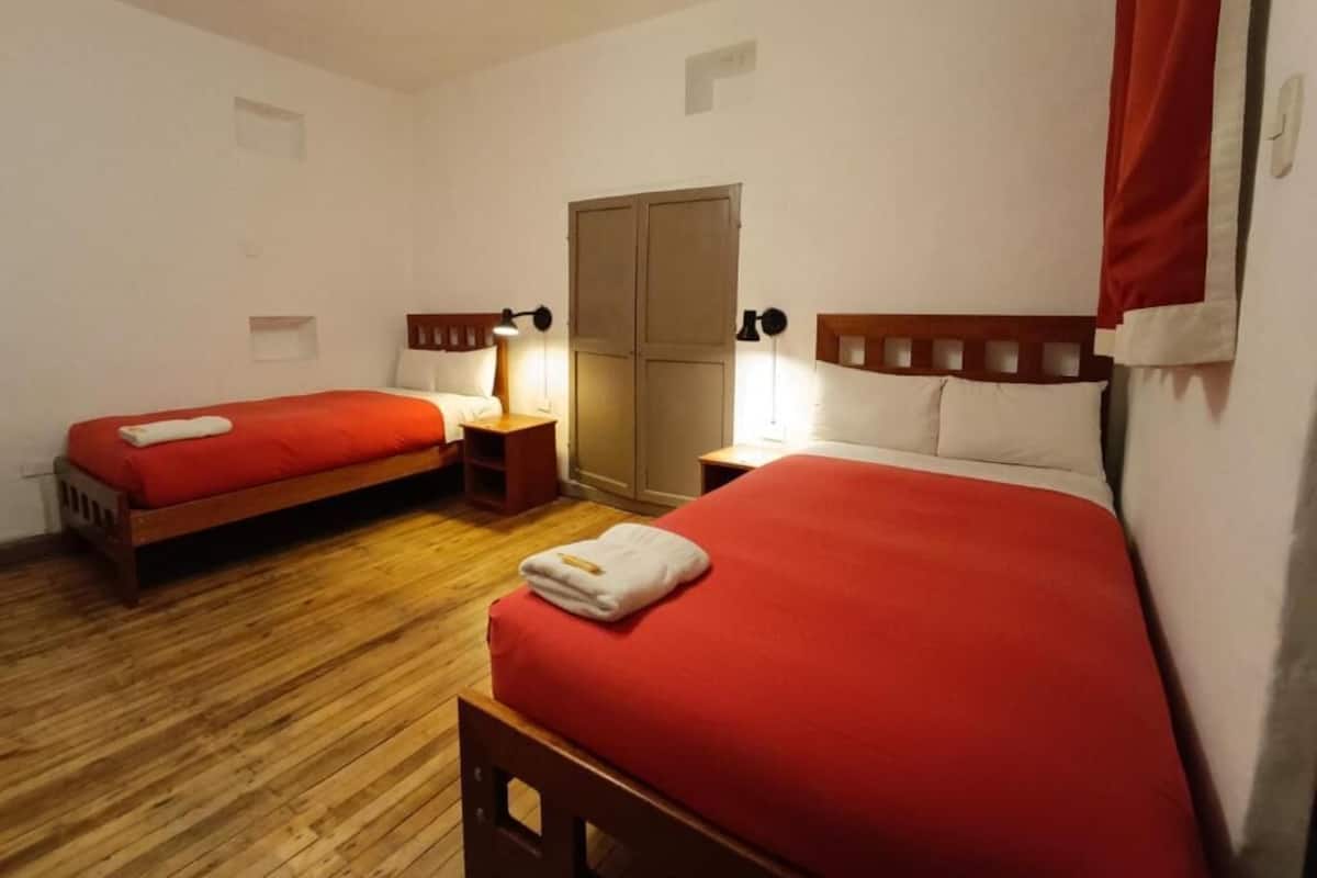 Una habitación con dos camas, suelo de madera, un armario y lámparas de noche.