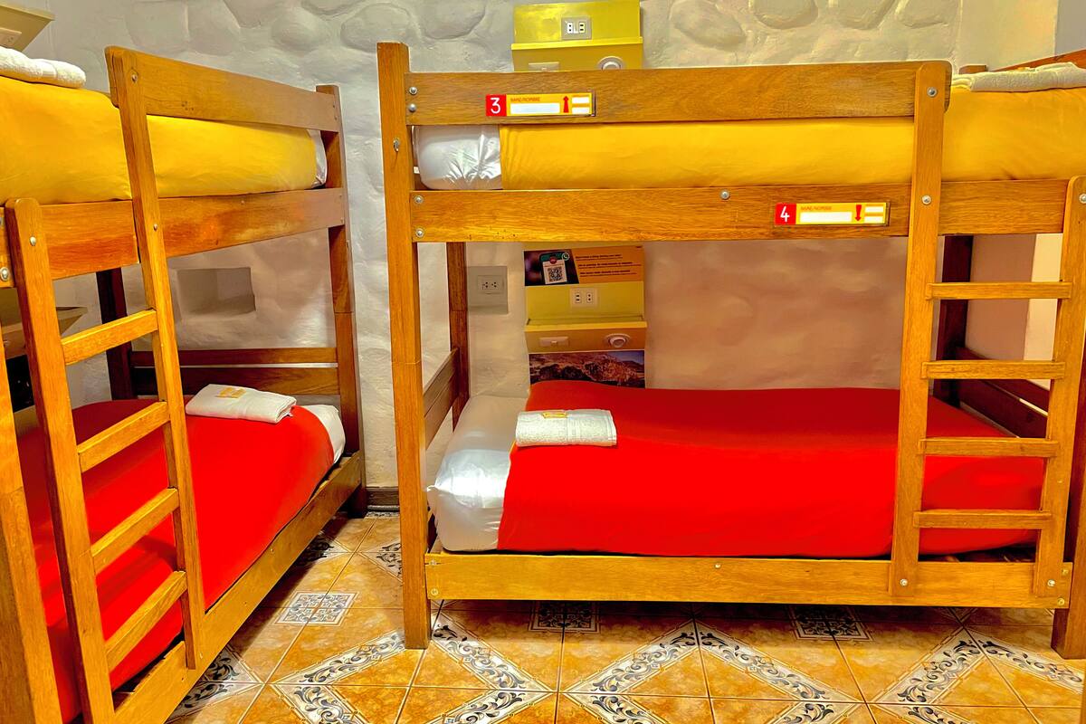 Dos camas literas con ropa de cama roja, una lámpara amarilla de pared y un suelo estampado.