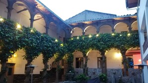 An outdoor seating area with tables and foosball tables, surrounded by stone walls and arches, with string lights overhead. - Pariwana Hostel Cusco - Adults only (Cusco)