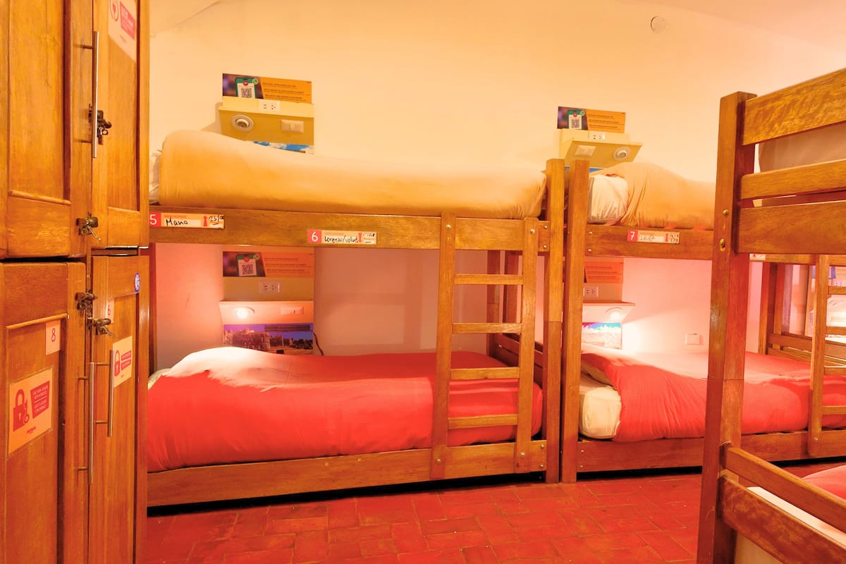 Habitación con literas de madera, letreros de habitación numerados y piso cubierto con alfombra roja.
