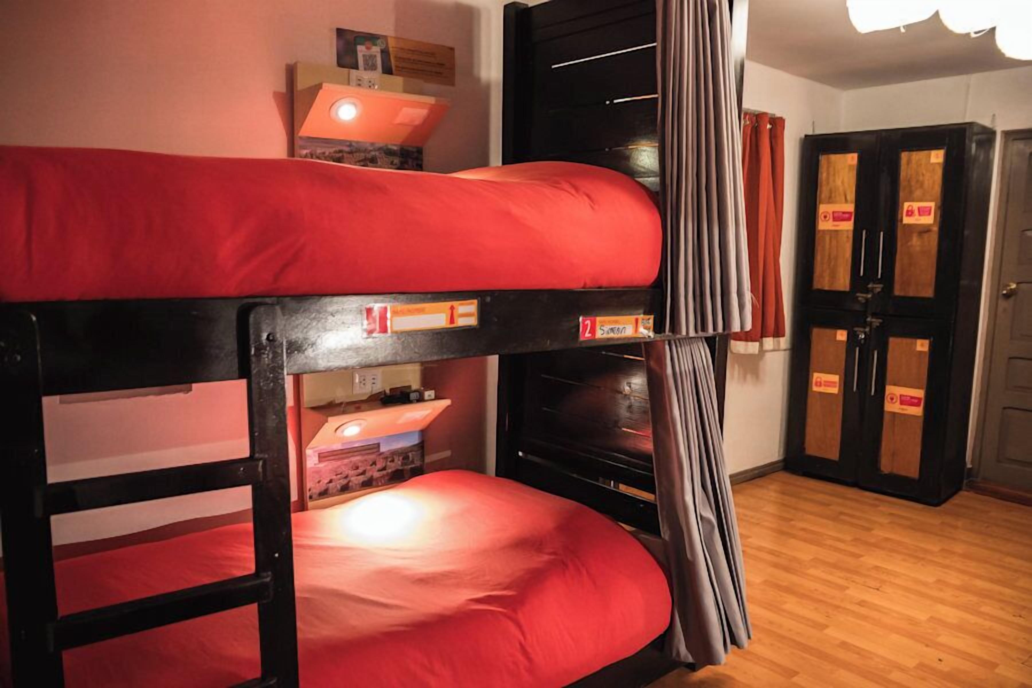 Un lit superposé avec une literie rouge, un plancher en bois, une armoire noire et une porte avec une pancarte.