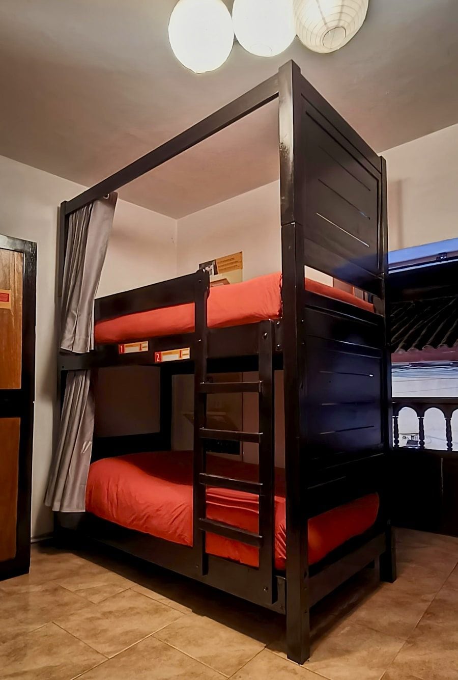 A bunk bed with a ladder, a curtain, and a wall-mounted light fixture.