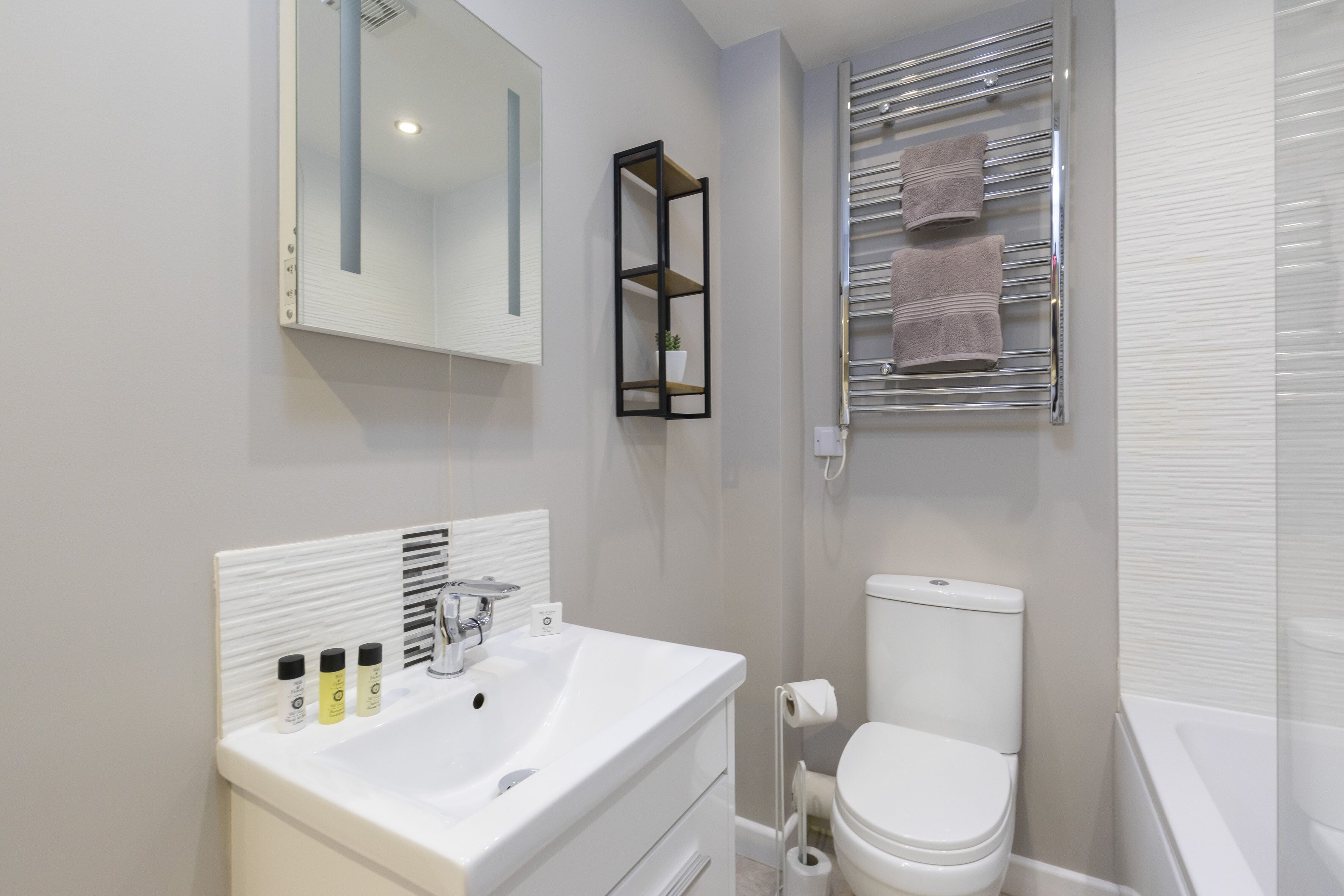 A modern bathroom with a white sink, a mirror, a toilet, and a towel rack.