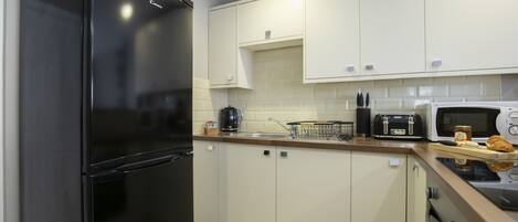 A modern kitchen with white cabinets, a black refrigerator, a microwave, a toaster, and a coffee maker.