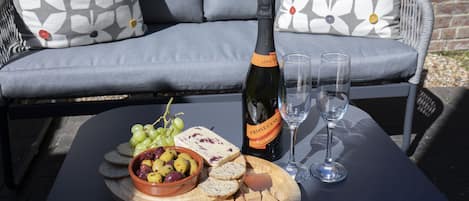 Une table avec une bouteille de prosecco, deux verres, un bol d’olives, des raisins et du fromage, le tout disposé sur une planche en bois.