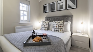 A neatly arranged bedroom with a bed, bedside table, and a window. - Elliot Oliver - 2 Bedroom Garden Apartment With Parking (Cheltenham)