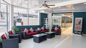 A modern hotel lobby with a seating area featuring wicker furniture and red cushions, glass-top tables, and a ceiling fan. - Hotel Milan Costa Rica (San José)