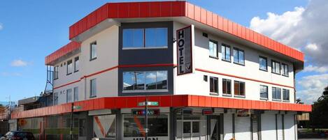 Ein zweistöckiges Hotel mit roter und weißer Fassade, einem gut sichtbaren Eingang und einem Schild für das 'Milan Hotel'.
