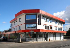 Un hotel de dos pisos con fachada roja y blanca, una entrada visible y un letrero que dice 'Milan Hotel'.