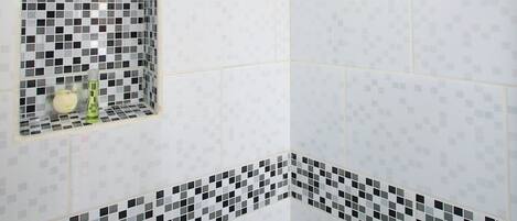 A shower with a handheld rainhead, a small window with a checkered pattern, and a tiled wall with a black and white border.