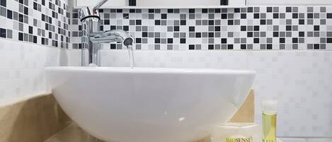 A white vessel sink with running water, a soap dispenser, and a bottle of liquid soap on a beige countertop.