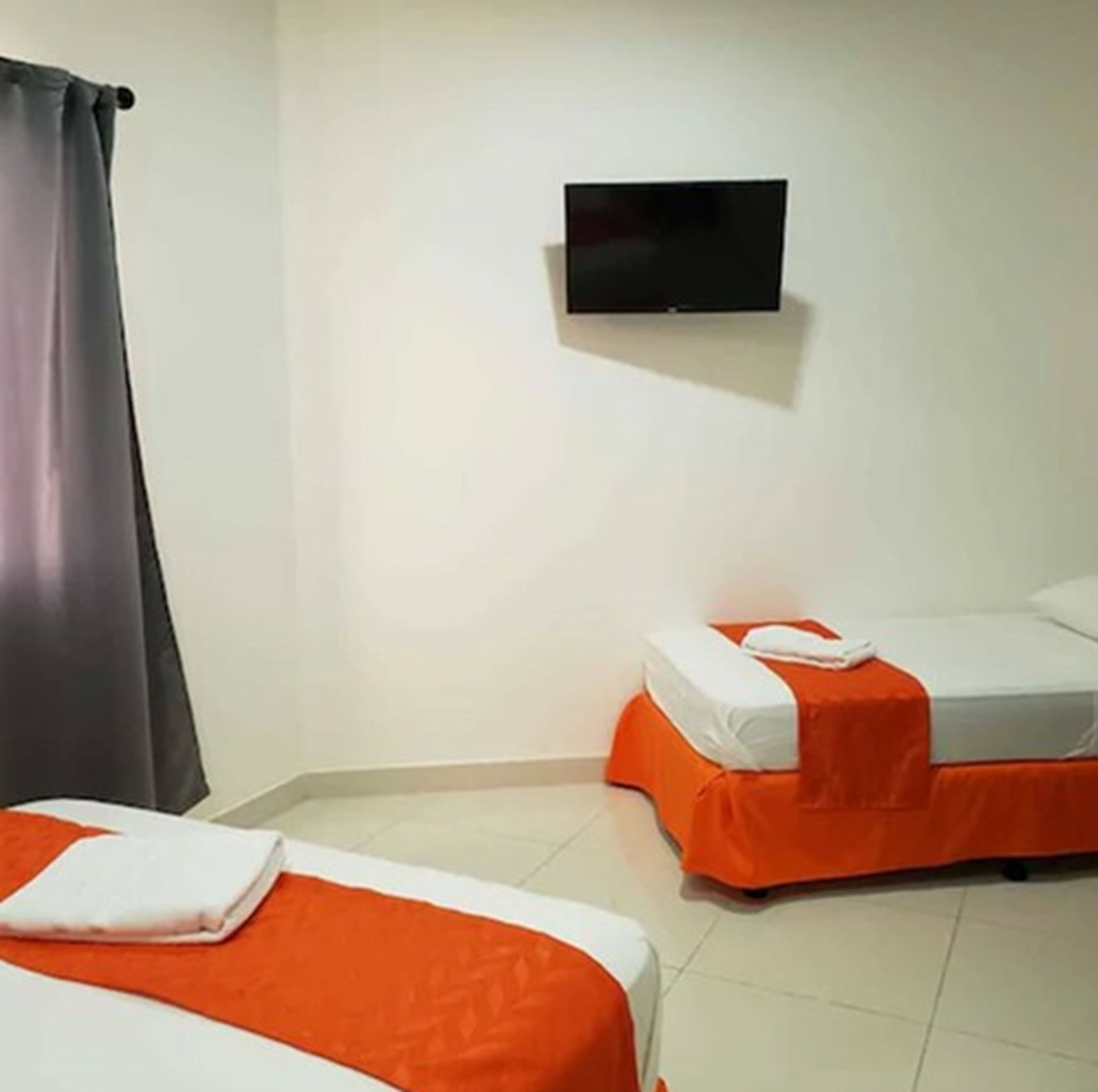 Quarto de hotel com duas camas, uma TV de tela plana na parede e uma cortina na janela.