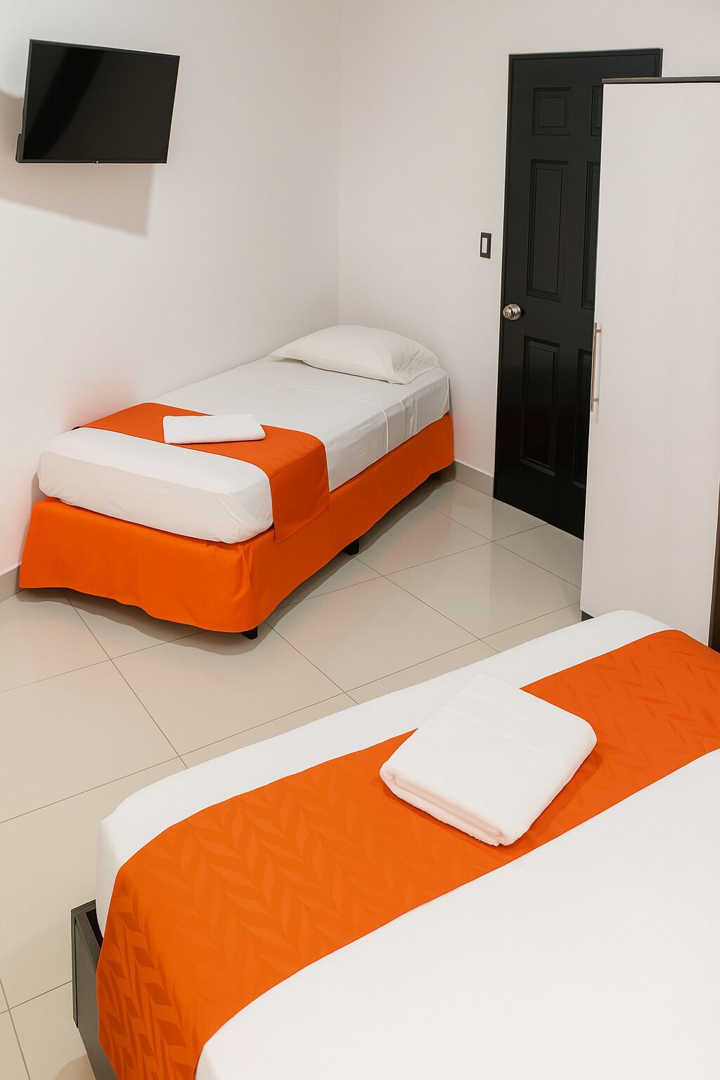 A hotel room with two beds, one with orange bedding and the other with white bedding. There is a TV mounted on the wall above the beds.