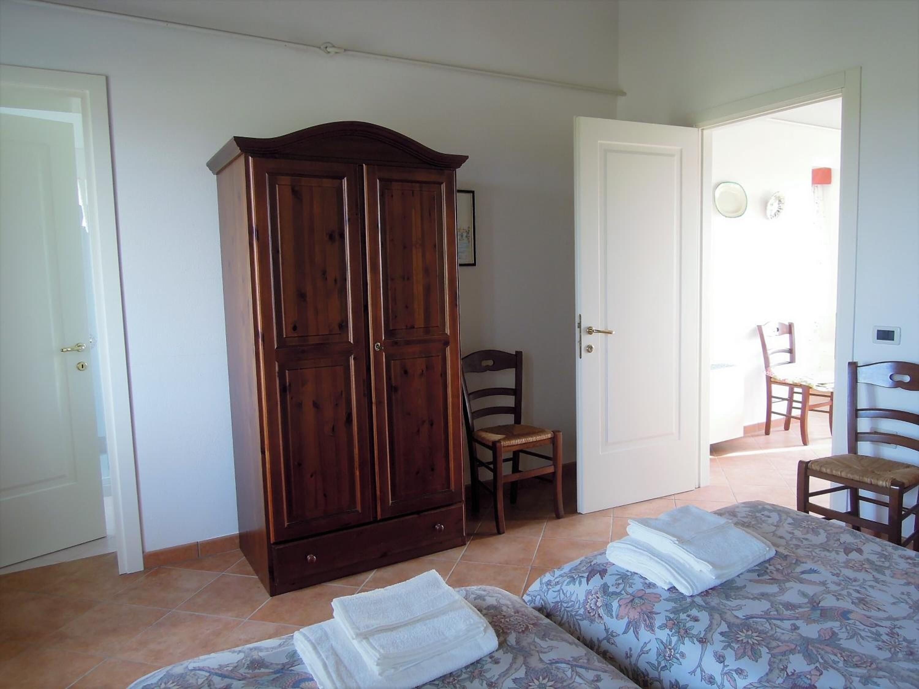 A bedroom with two beds, a wardrobe, and a chair.