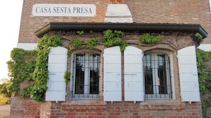 A building with a sign reading "CASA SESTA PRESA" and a brick facade with white shutters and vines growing on the side. - Agriturismo Sesta Presa (Caorle)