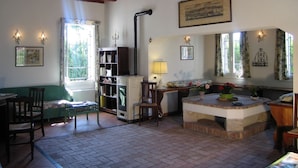 A cozy living room with a fireplace, wooden beams, a green sofa, a wooden table, and a bookshelf. - Agriturismo Sesta Presa (Caorle)