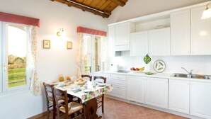 A kitchen with white cabinets, a dining table with chairs, and a window with curtains. - Agriturismo Sesta Presa (Caorle)