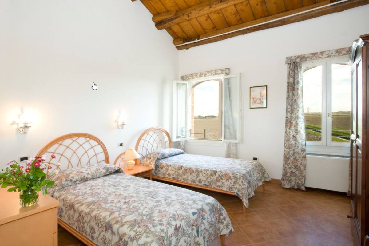 Ein Schlafzimmer mit zwei Einzelbetten, einer Holzbalkendecke, einem Fenster mit Vorhängen und einem Nachttisch mit Lampe.