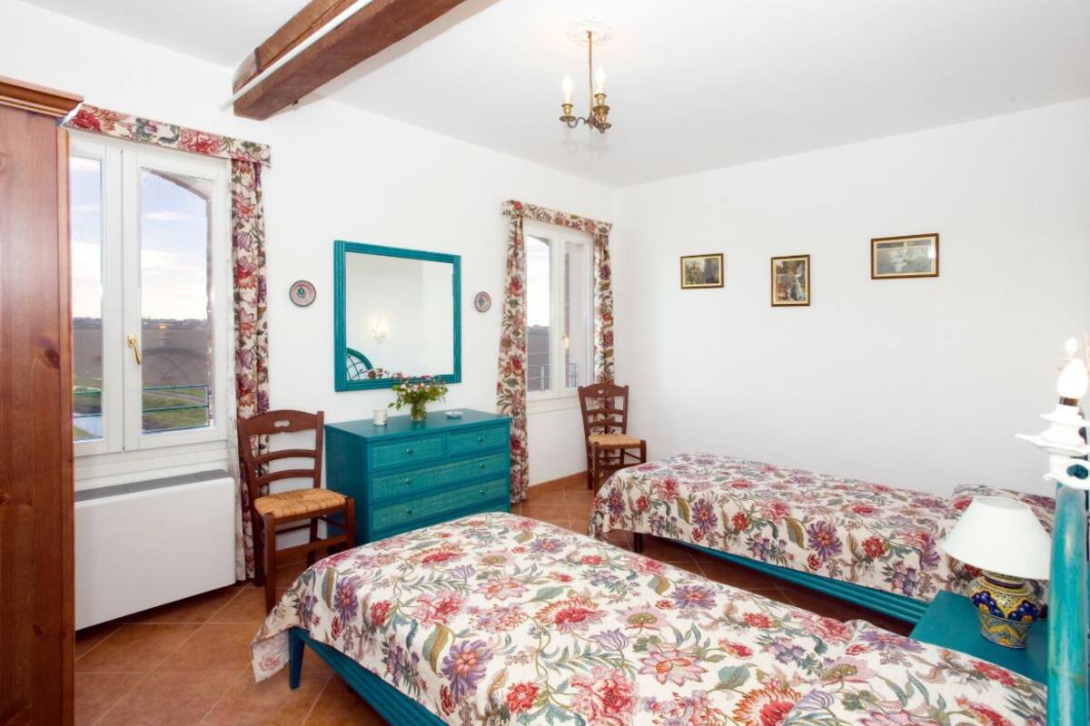 Ein Schlafzimmer mit zwei Betten, einem Schminktisch, einem Stuhl, einem Spiegel und einem Fenster mit Vorhängen.