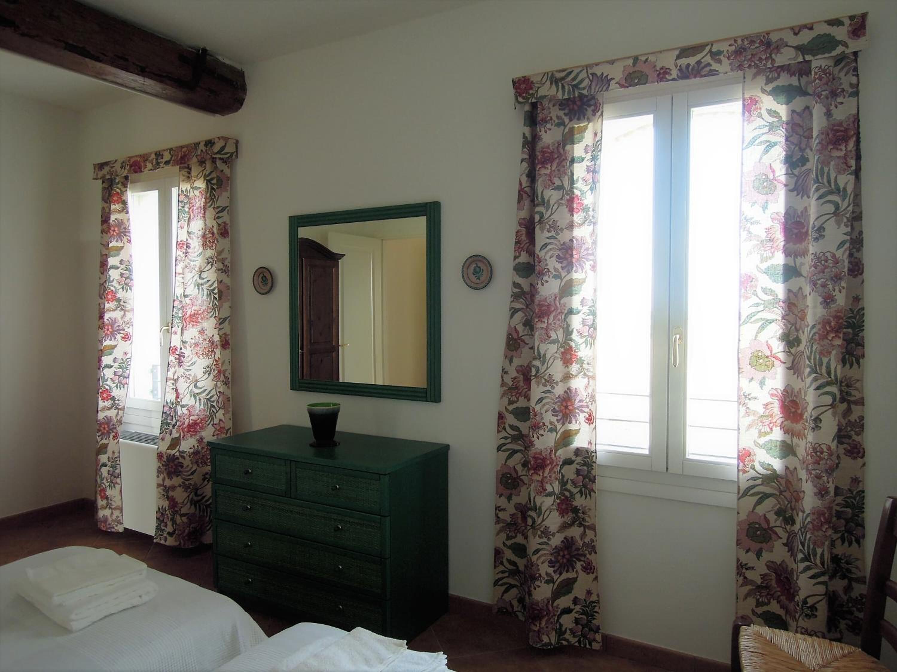A bedroom with a bed, a dresser, a mirror, and floral curtains.