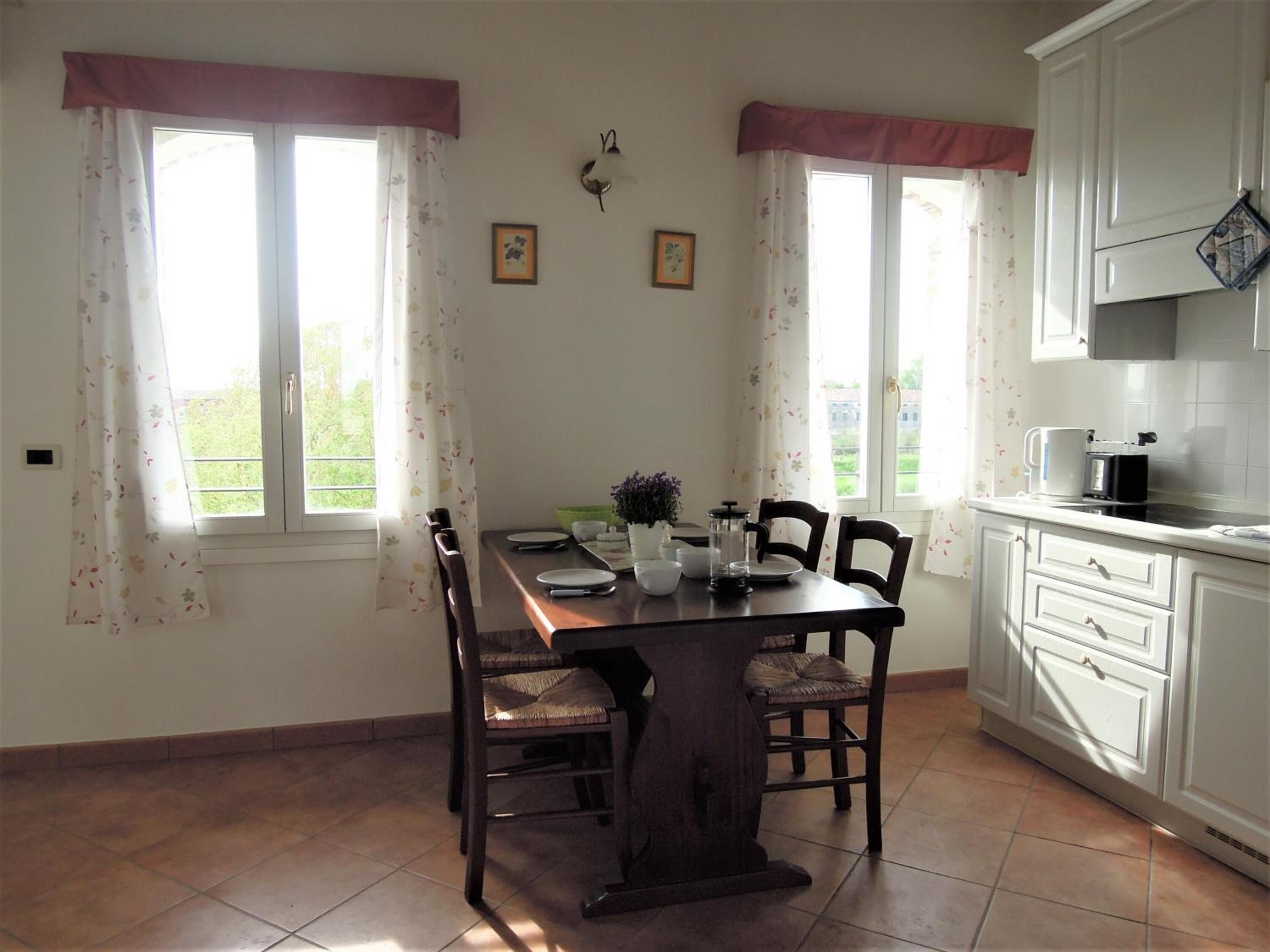 A dining area with a wooden table, four chairs, a coffee maker, and a window with curtains.